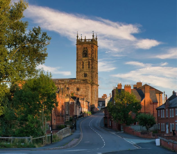 Whitchurch. A road in the centre, with houses on the right and trees and the church on the left.