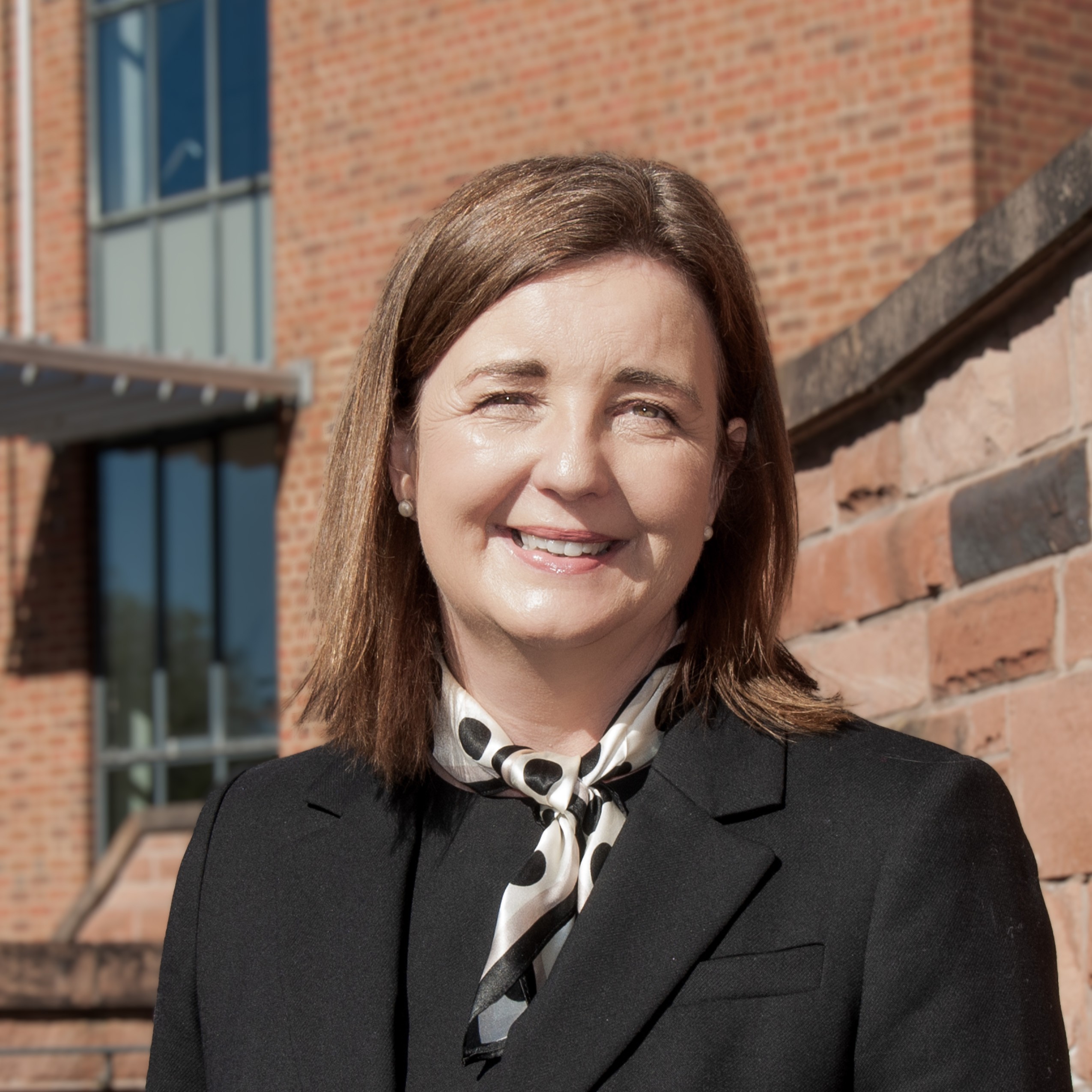 A woman smiling into the camera with a building in the background.