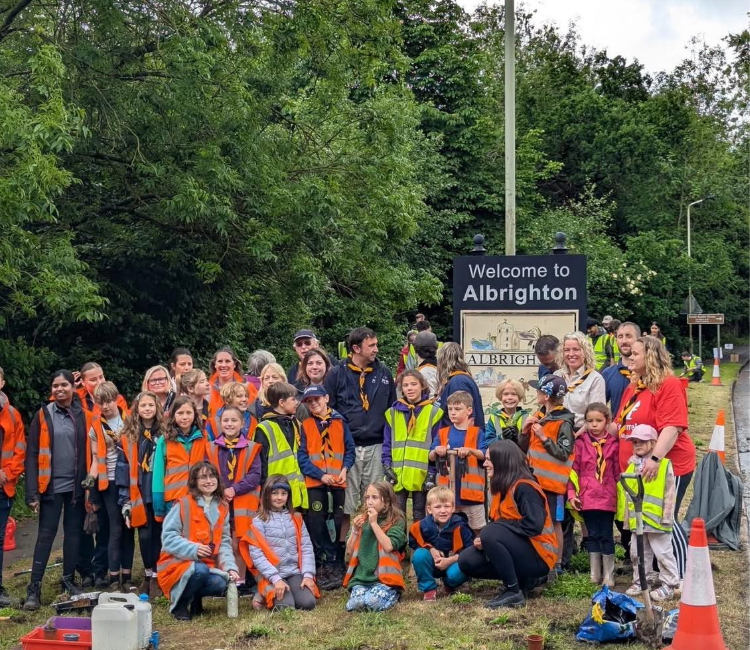 A large group of children and adults around a sign which reads 'Welcome to Albrighton'